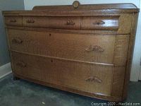 Front view of vintage tiger oak dresser showing five drawers with distinctive wood grain and carved wooden handles with shell or wing motifs.