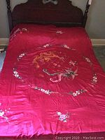 Top view of the bedspread laid on a bed showing the red satin fabric and embroidered circular floral pattern in the center with additional floral embroidery on the sides.