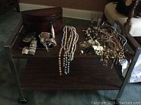 Table with jewelry items arranged on top including bead necklaces, earrings, rings, and jewelry box.