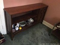Front view of wooden shelf showing two open shelves on left, enclosed shelves with paneled doors on right, placed against wall on carpeted floor.