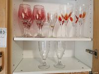 Front view of all glasses on shelf showing six glasses with red spots, two small glasses with gold design, and two larger clear textured glasses.