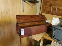 Front view of rectangular wooden box with hinged lid closed, showing wear on wood and metal hinges.