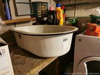 Large white enamel wash basin on wooden table with black rim and sticker label visible.