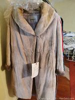 Front view of a vintage Persian lamb fur coat in beige/cream color with darker brown shirred muskrat cuffs, hanging on a rack.
