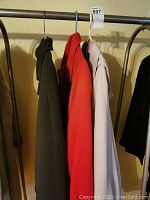 Three ladies jackets hanging on a rack: red wool, olive green wool, beige London Fog.