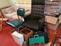 Photo of green and black office chairs, wooden box, shredder, fan, and briefcases in front of a couch and carpet.