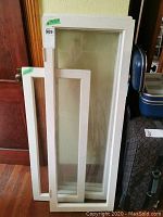 Assorted white wooden framed glass windows leaning against a wall near a wooden door, showing size and condition