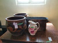 Three outdoor planters, copper ash holder, and ceramic pitcher on table under window.