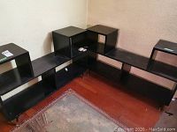 Two black modular shelving units arranged in an L-shape, showing multiple open compartments and surface wear.