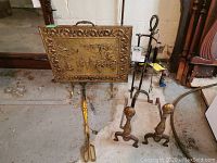 Front view of brass fire screen, fireplace tool set stand, brass andirons, and yellow log holder on concrete floor