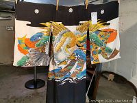 Front view of kimono hung showing black upper section with family crests and multicolor eagle design on white and black fabric