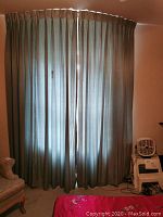 Front view of the pair of blue lined pleated drapes covering a window, showing pleated detailing and light filtering through fabric.