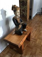 Wooden bench with natural finish and carved Thai wooden figure seated on top