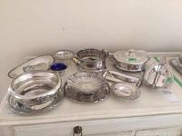 Photo showing an assortment of silverplate serving dishes and plates on a white dresser top with clear and cobalt blue glass bowls.