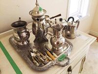 Wide view of silverplate tea set, tray, and flatware with visible tarnish and distinctive wooden handles on some pieces.