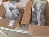 Two open boxes with crystal stemware glasses wrapped in tissue paper, showing clear glassware of different shapes and sizes.