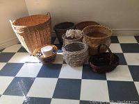 Seven baskets and two ceramic planters displayed on a checkered floor, showing size and color variety.