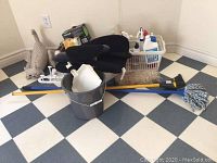 Photo showing mop bucket, mop, broom, dust pan, duster, back support cushions, and cleaning products in plastic basket