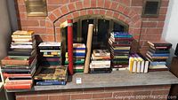 Collection of stacked books with Bible chronology scrolls standing in the center with wooden ends, displayed on a fireplace hearth