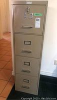 Full view of the tall beige metal filing cabinet with four drawers and label holders