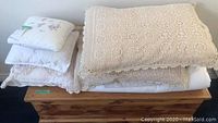 Stack of pillows with white and beige crochet covers on wooden surface