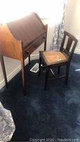 Photo showing the vintage escritoire writing desk and small wooden chair with cane seat, positioned by the window on carpet.