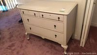 Front view of vintage off-white painted wood dresser with four drawers, metal handles, and casters on bottom.