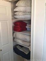 Shelves with folded white pillows, red linens, and white linens