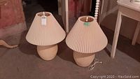 Pair of matching table lamps with pleated beige/off-white fabric shades and round ribbed ceramic bases, each about 27 inches tall. Both lamps have white power cords attached.