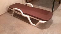 White resin patio lounger with a fitted brown cushion placed on top, viewed from the side showing the cushioned surface.