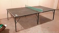 Full view of the wooden ping pong table with green net set up indoors, showing folding center hinge and metal legs.