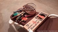 Sports equipment including ping pong paddles, balls, net, vintage tennis rackets, Prince aluminum tennis racket and boxed badminton rackets on outdoor chair