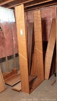 Disassembled vertical solid wood shelving panels standing upright in basement.