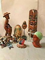 Full lot showing all 8 items including carved wooden statues, mask, ceramic head, figurines, glass cross, and prayer plaque.