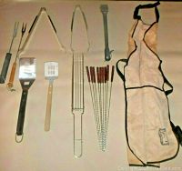 Full lot displayed including apron, skewers, spatulas, forks, tongs, kabob basket, and grill brush.