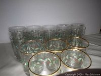 Set of 14 rocks glasses decorated with holly berry design, arranged in two rows with front row showing gold rims clearly.