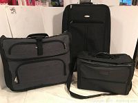 Three pieces of luggage: large black Samsonite suitcase, grey Travel Select bag, small black filing carrying bag