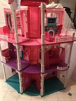 Full view of the three-floor Barbie Dream House showing the exterior structure, floors, balconies, and elevator shafts in the center