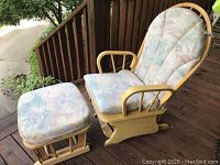 Photo showing wooden cushioned glider chair with matching footrest outdoors on a wood deck.