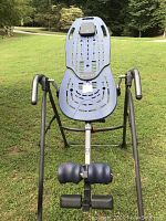 Full view of Teeter inversion table showing blue ergonomic bed with ventilation slots and adjustable black handles, on metal stand, outdoors.