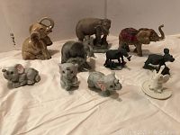 10 elephant figurines assorted in two rows on a white cloth, showing different styles and sizes.
