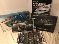 Full view of boxed tabletop games and toys including Air Hockey, billiards, Laser-X laser tag, foosball, and Sky-Viper drone