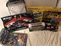 Full lot shown including boxed Stanley Jr. tool set, Zuru X-Shot laser tag, Tek-Force robots, pullback and remote control cars, pinball game.