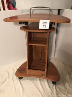 Side view showing the top desk surface with metal handle and lower shelves, brand label visible on base shelf