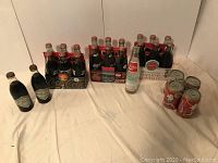 Wide shot of entire Coca Cola memorabilia collection showing two black label bottles, multiple six-pack bottles, and several cans.