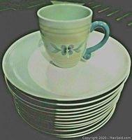 Stack of 12 cream colored dinner plates with subtle stripe pattern and a Summer Breeze mug on top.