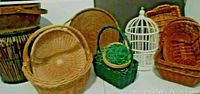 Photo showing various woven baskets and trays along with a white decorative bird cage on a white surface with dark background.