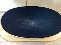 Oval large metal bowl with deep blue textured enamel interior and beaded white rim on light floor.
