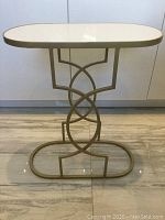 Front view of modern side table with white granite top and gold metal base with intricate circular design.