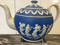 Full side view of blue jasperware teapot with white Neoclassical figures on one side, decorative frieze on lid